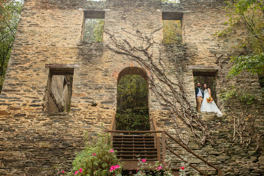 Best All-Inclusive Wedding Venue in Georgia: Hightower Falls. Historic ruins by a wedding waterfall, bride and groom in luxury designer wedding dress & suit pose for photos near an outdoor wedding ceremony