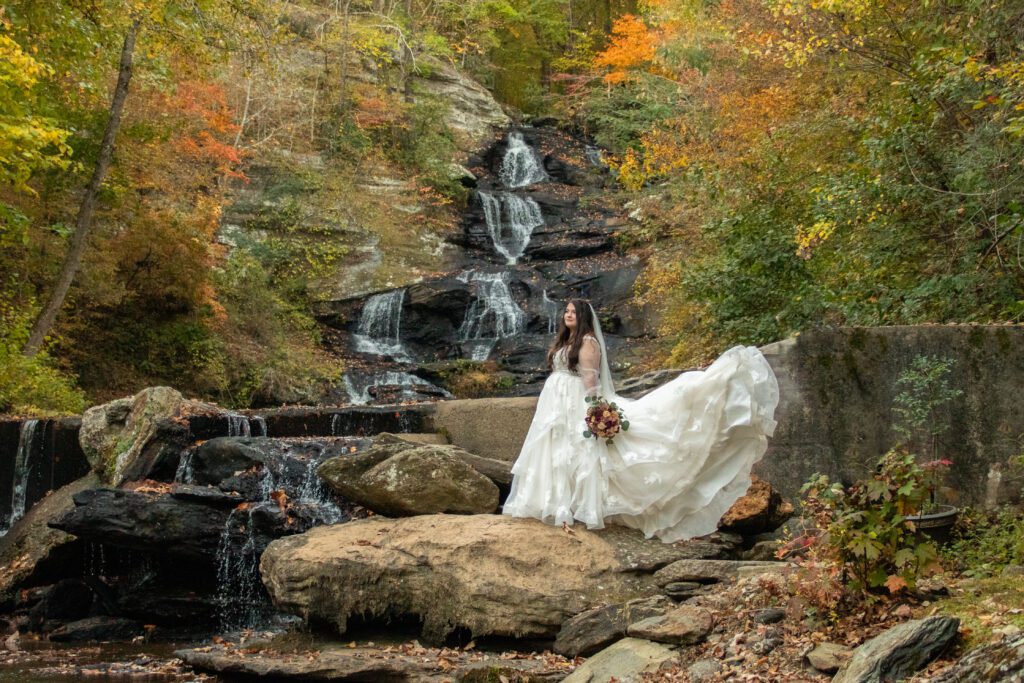 Best All-Inclusive Wedding Venue in Georgia: Hightower Falls. Historic ruins by a wedding waterfall, bride in luxury designer wedding dress poses by a waterfall near an outdoor wedding ceremony during fall near Atlanta Georgia