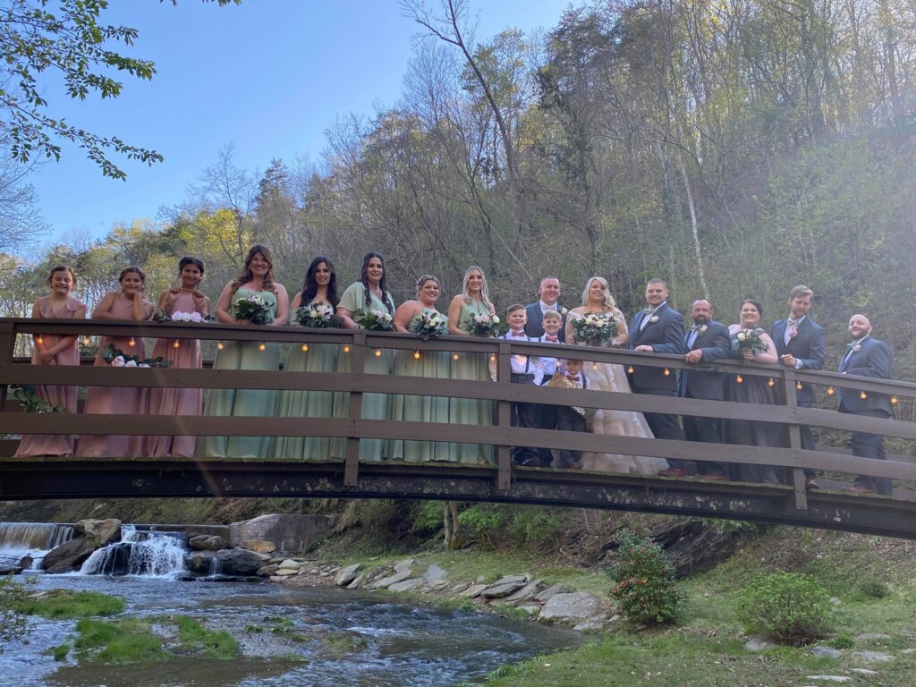 Brides, groom, bridesmaids and groomsmen pose for photos on a bridge with a waterfall backdrop wedding venue near Atlanta